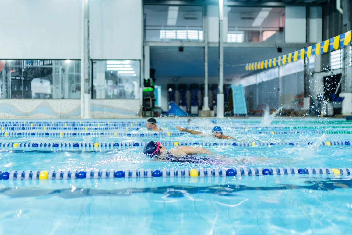 Swimmers practicing in a school swimming pool, surrounded by sports equipment designed for educational use.