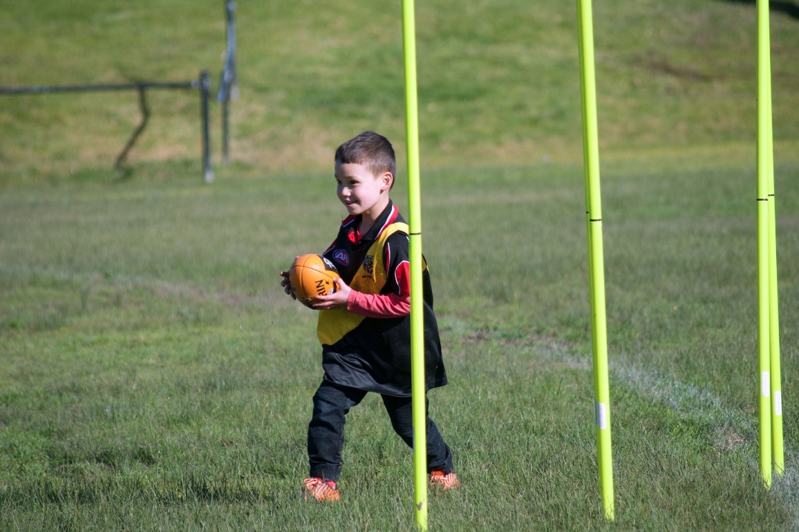 A young boy stands in a field, confidently holding a football, showcasing sports equipment for school children.