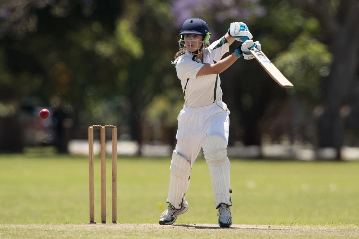 A female cricket player skillfully batting on a field, showcasing athleticism and sportsmanship in school sports.