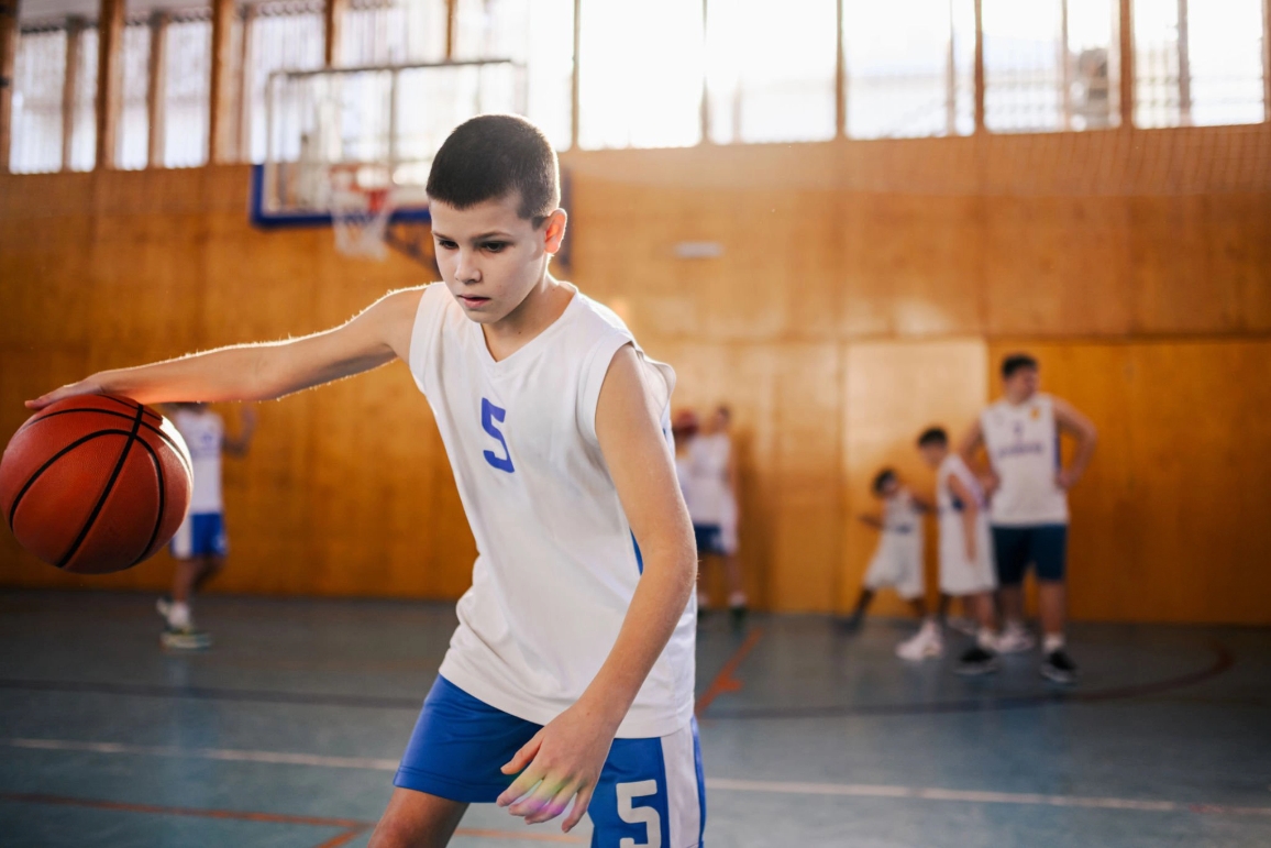 A young boy dribbles a basketball in a gym, highlighting the importance of sports equipment for children's physical activity.